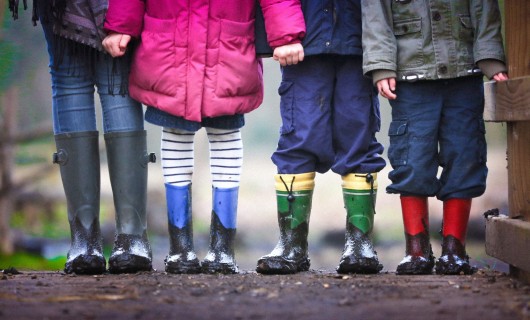 Vier Kinder tragen Gummistiefel und stehen in der Natur.