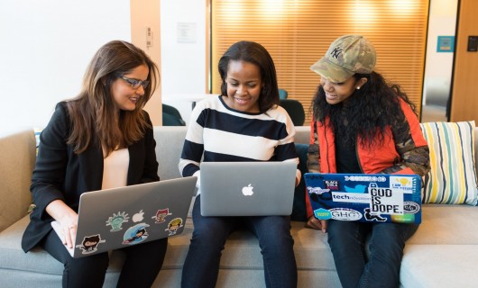 Drei Frauen sitzen zusammen auf einem Sofa und arbeiten auf ihren Laptops.