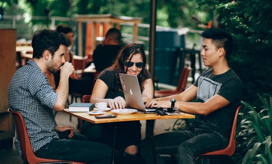 Drei junge Menschen sitzen zusammen in einem Cafe und arbeiten an einem Laptop.